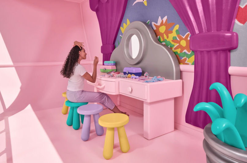 a photo of a model posing at the life-sized Polly Pocket vanity, from the Polly Pocket experience offered by Airbnb